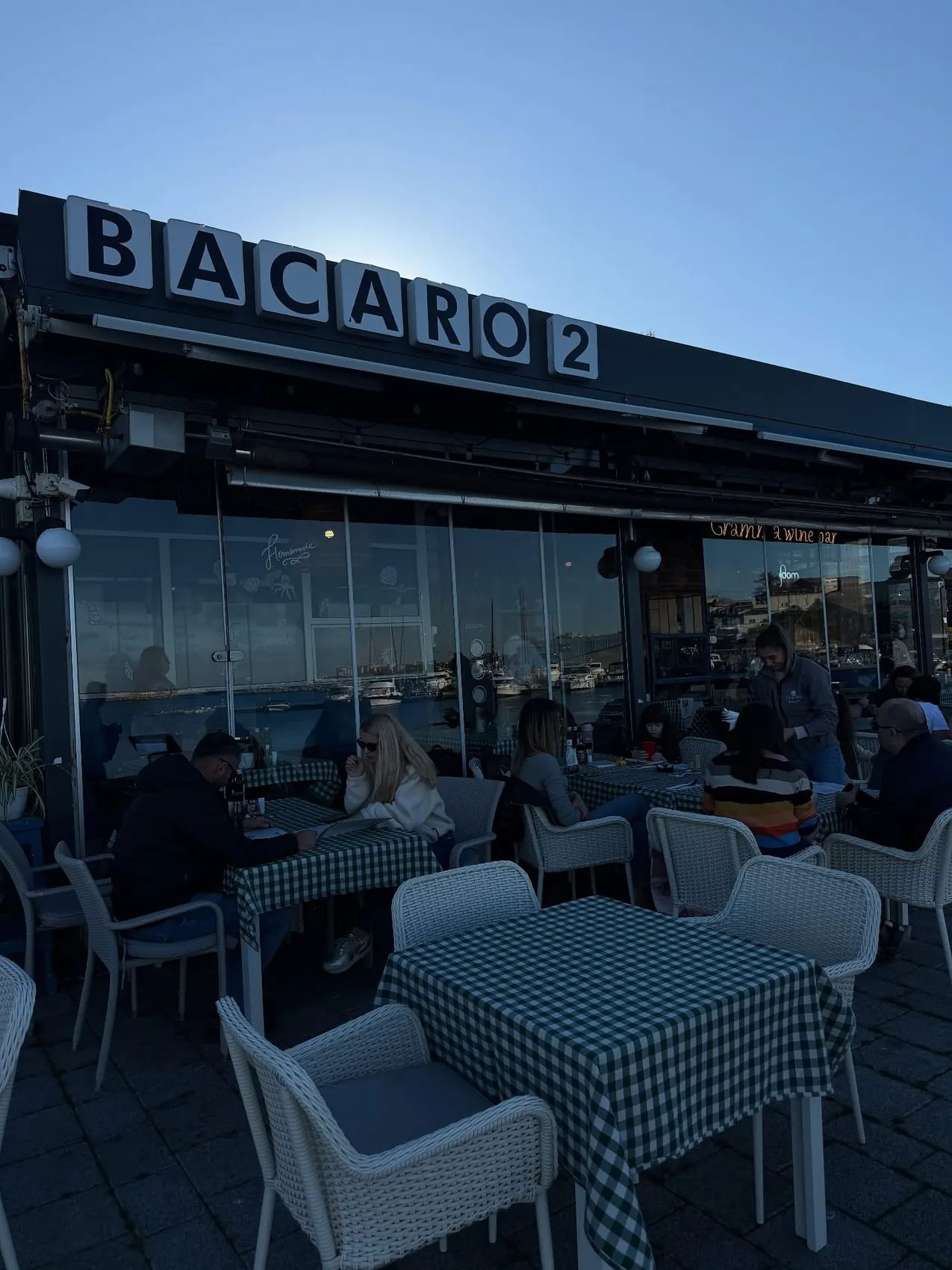 Fațada Bacaro 2 cu mese în carouri verzi și terasa spre port
