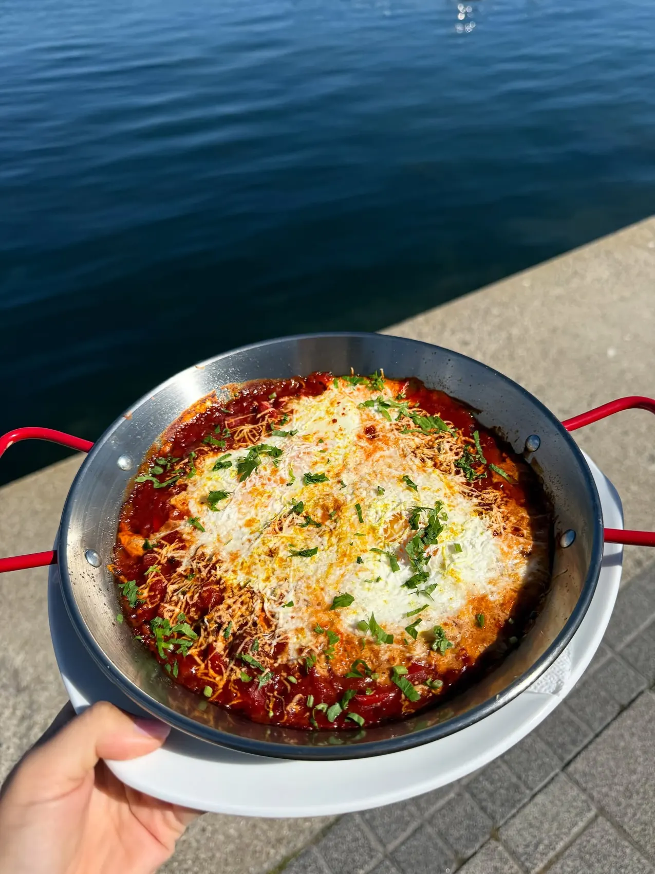 Shakshuka într-o tigaie, ținută în mână pe chei