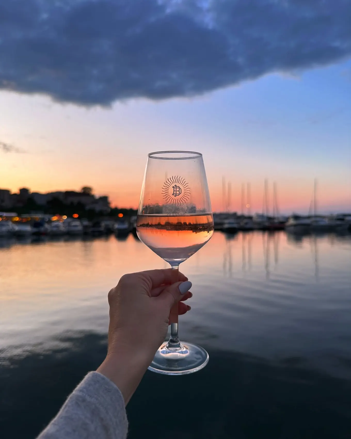 Pahar de vin ridicat în fața unui apus roz peste port